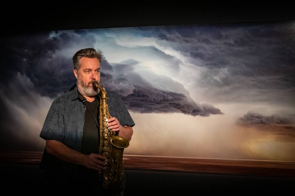 Spike Mason plays his saxophone in front of photomedia by Murray Fredericks on display at the QVMAG. Picture by Paul Scambler