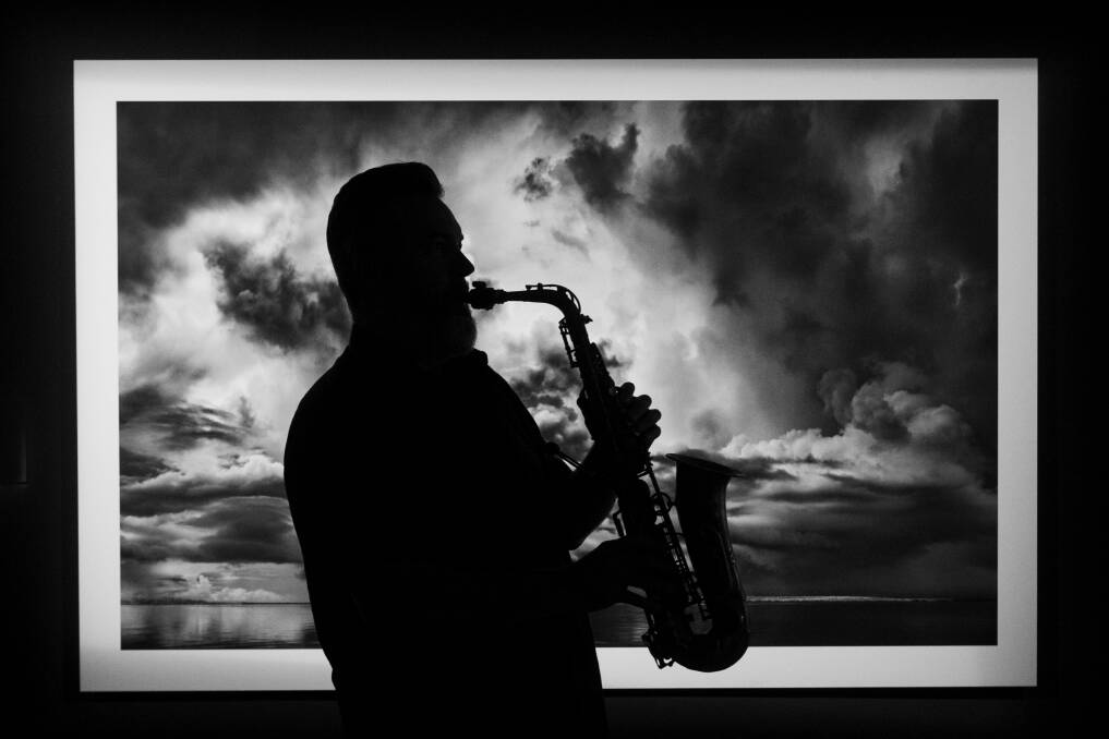 Spike Mason plays his saxophone in front of photomedia by Murray Fredericks on display at the QVMAG. Picture by Paul Scambler
