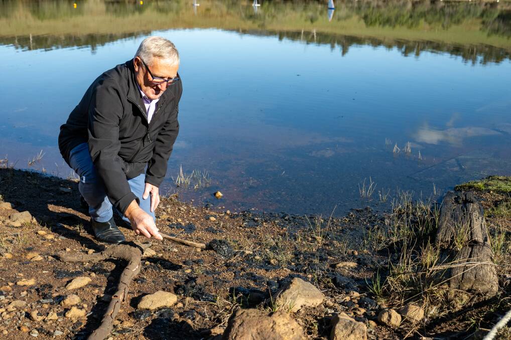Launceston Life Saving Club president Geoff Lyons with the black sludge on the end of a stick on the foreshore at Trevallyn Lake. Picture by Paul Scambler 