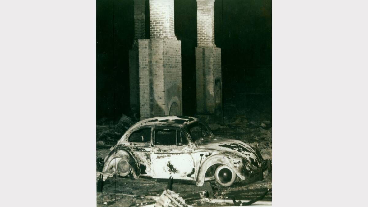 1967 Bushfires: The burnt-out shell of a Volkswagen in front of a group of tenement buildings in Waterworks Road, Dynnyrne.