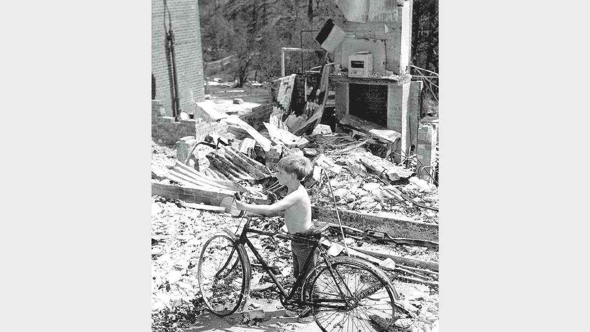 1967 Bushfires: Stephen Ward, 9 resurrects his bicycle from the ruins of his parent's home.